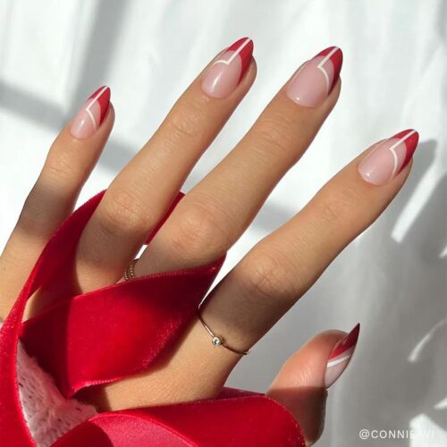 Hand with red and pink heart-themed nail art design, wrapped in a red velvet ribbon.