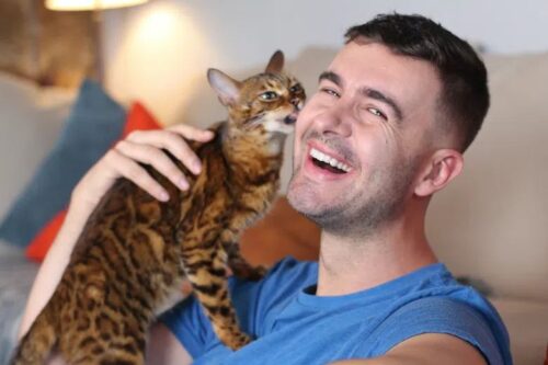 Cat licking a smiling man's face while he laughs.