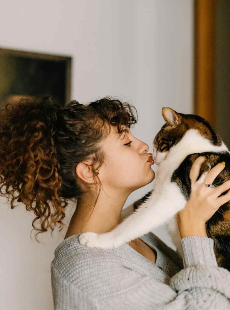 Woman holding and kissing her cat affectionately.