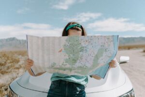 Woman reading a large map in front of a car in the desert.