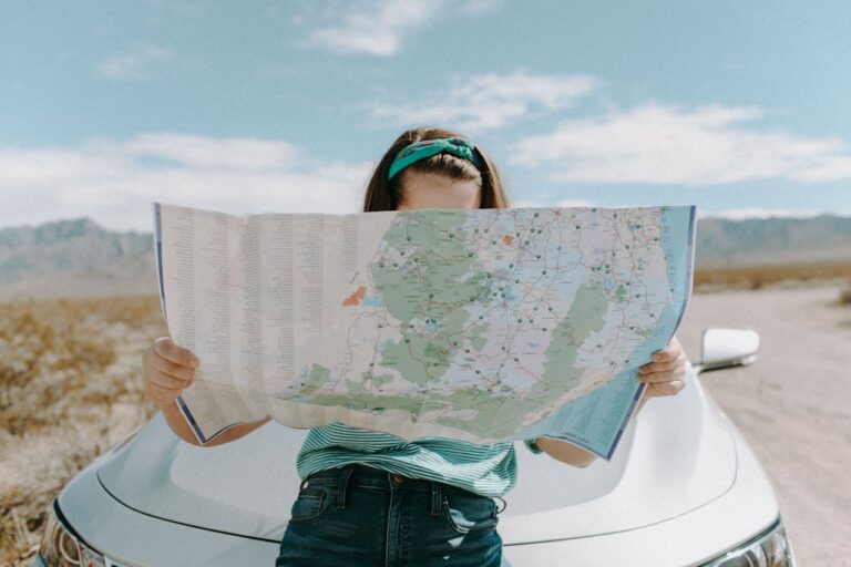Woman reading a large map in front of a car in the desert.