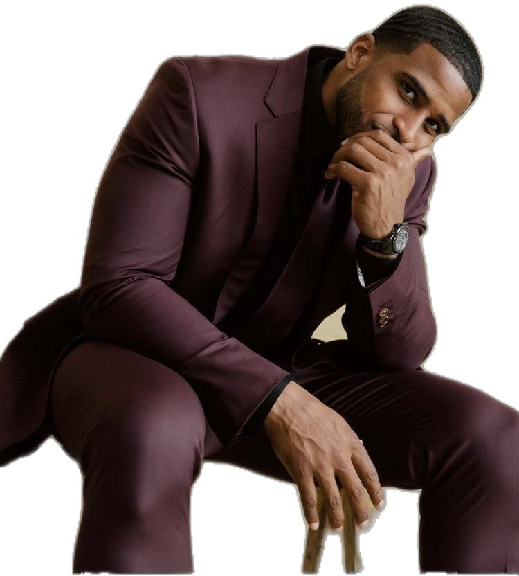 Bobby Wagner in a maroon suit sitting and leaning forward with his hand partially covering his face, looking thoughtfully at the camera.